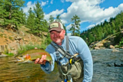 Bryan Donoway holds a just-caught trout under a blue sky with fluffy clouds.